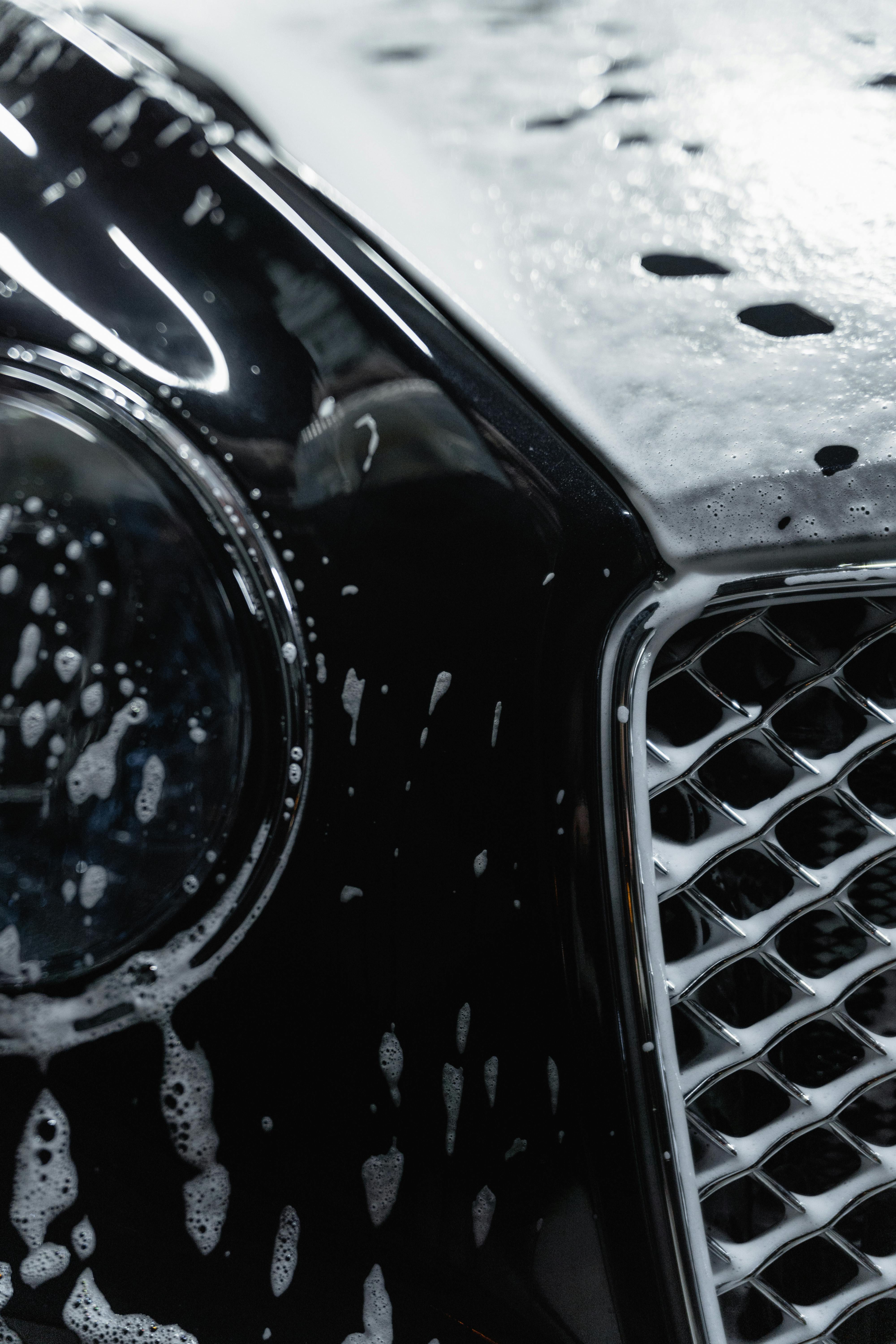 Professional hand washing a vehicle outdoors with rich soap suds